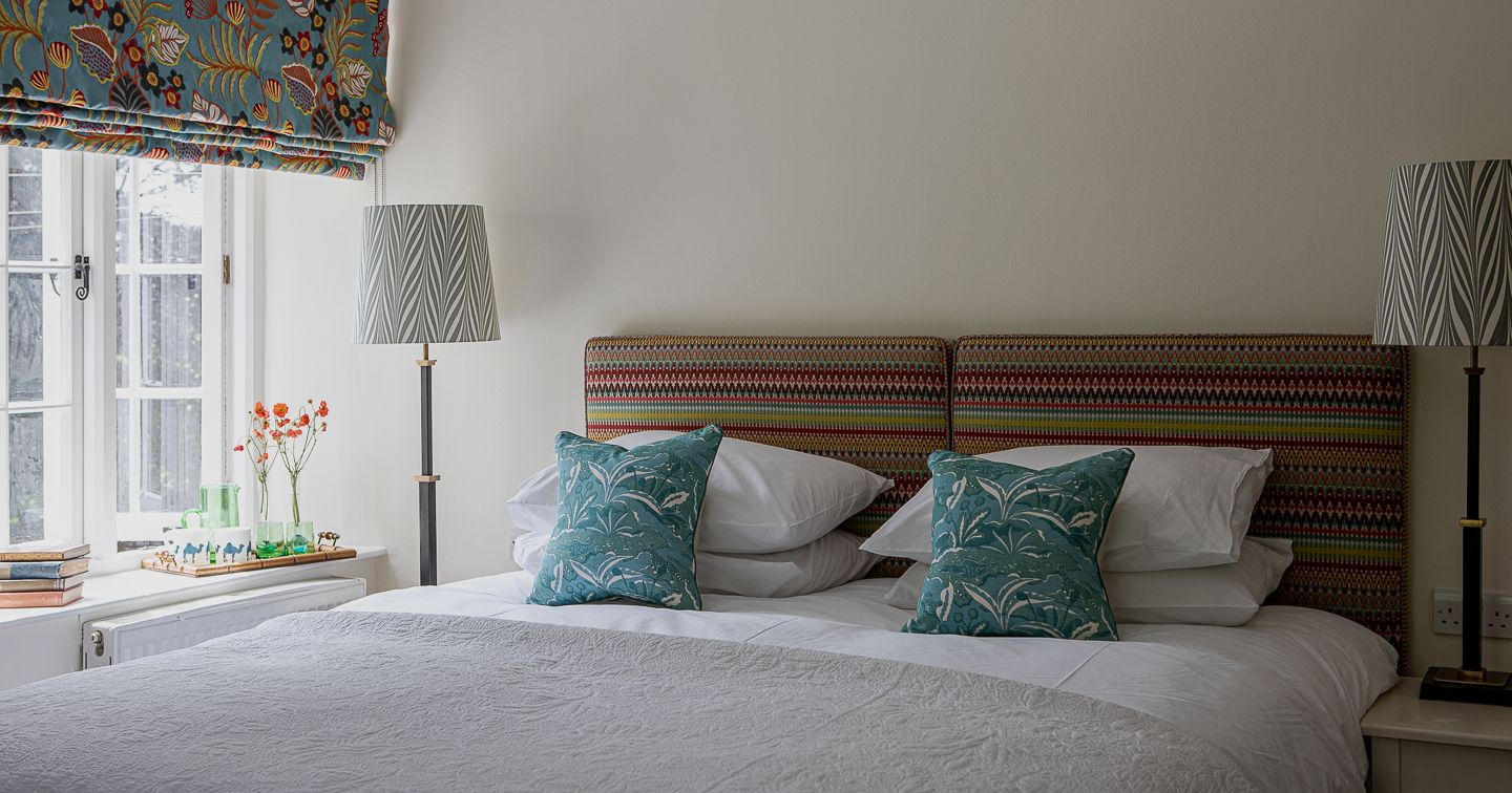 Cozy and colorful bedroom with patterned headboard, teal pillows, and large window with floral curtains