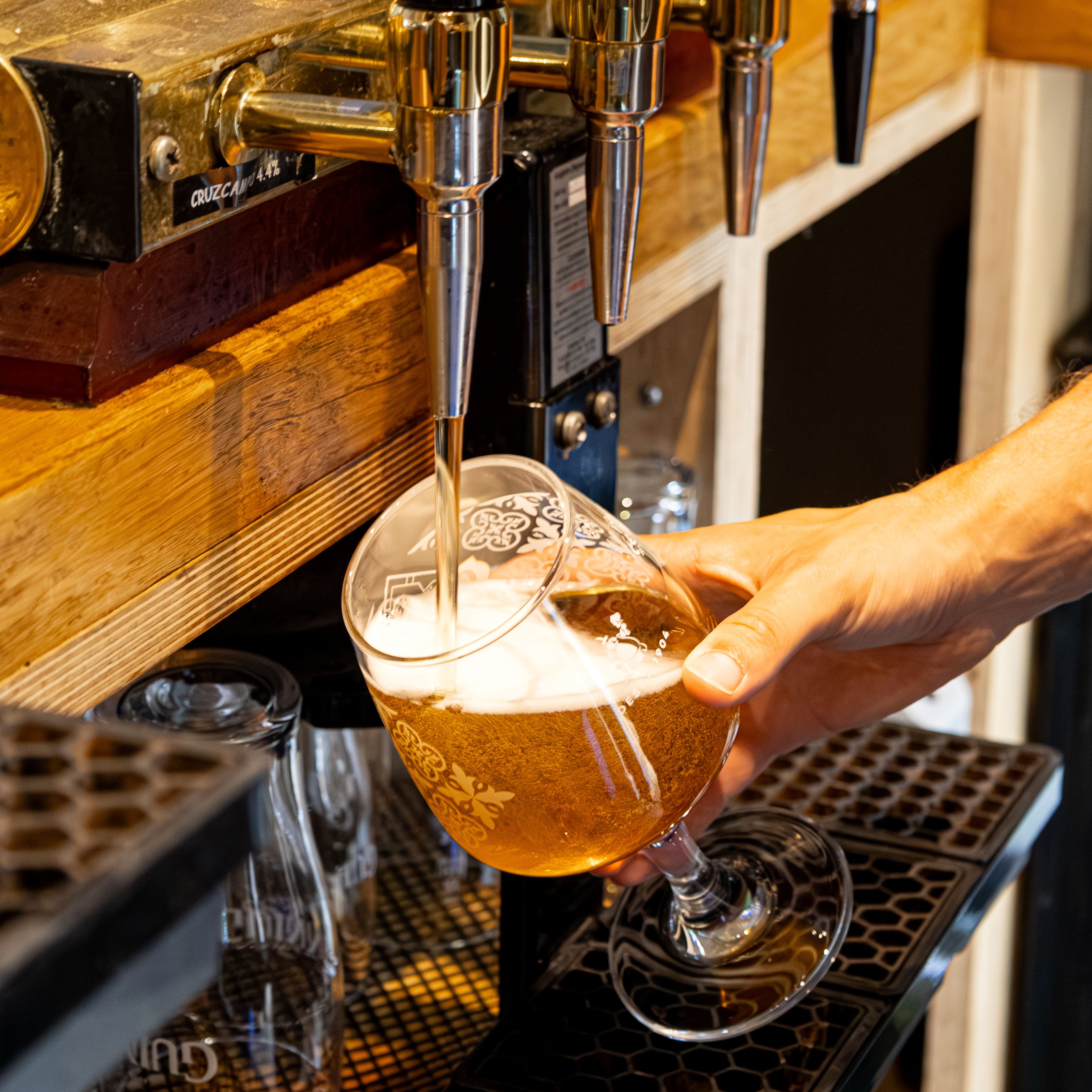 Hand pouring draft beer into a glass from a golden beer tap at a bar
