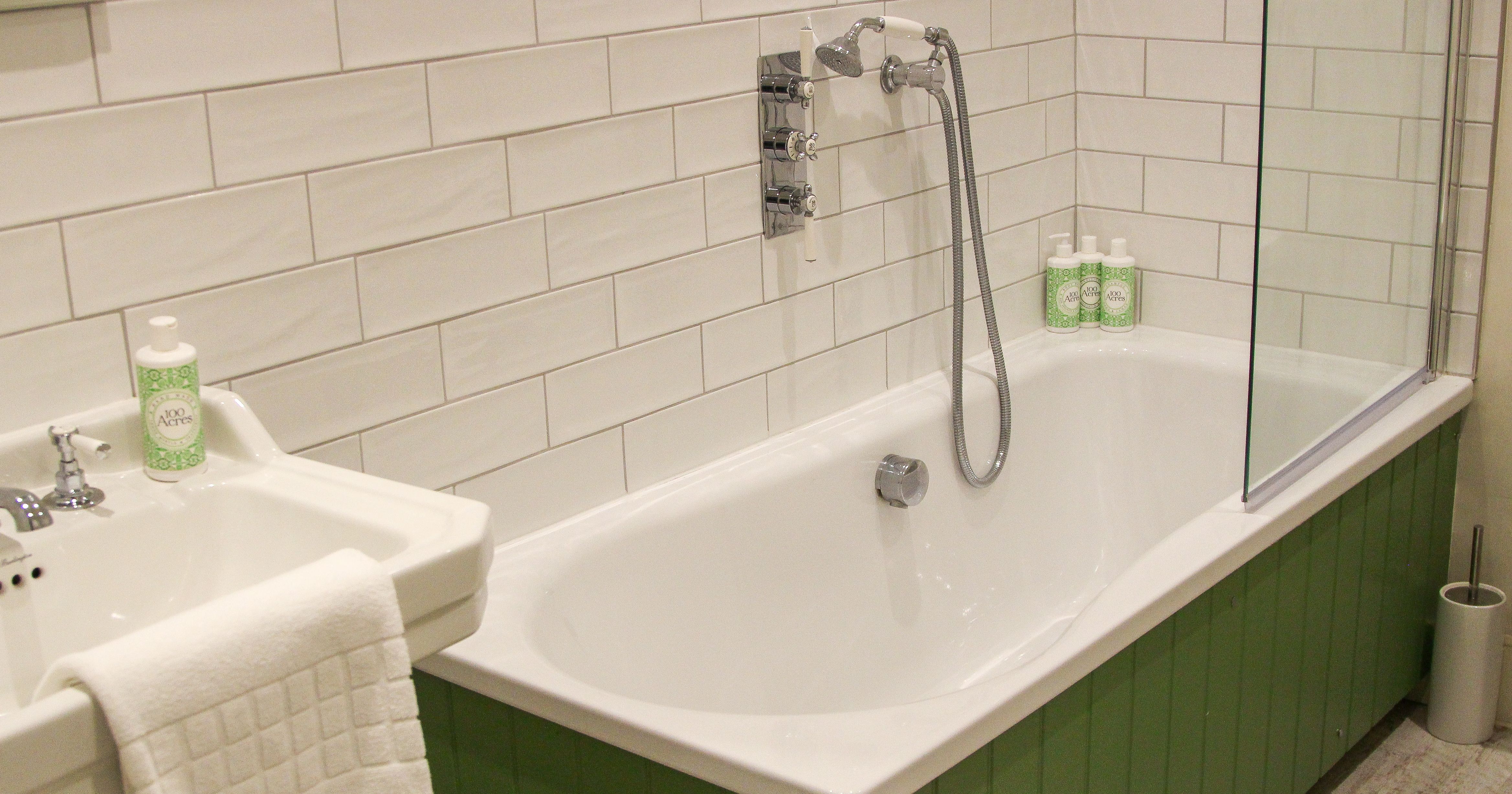 Modern bathroom with green panel bathtub, white tile walls, and sink