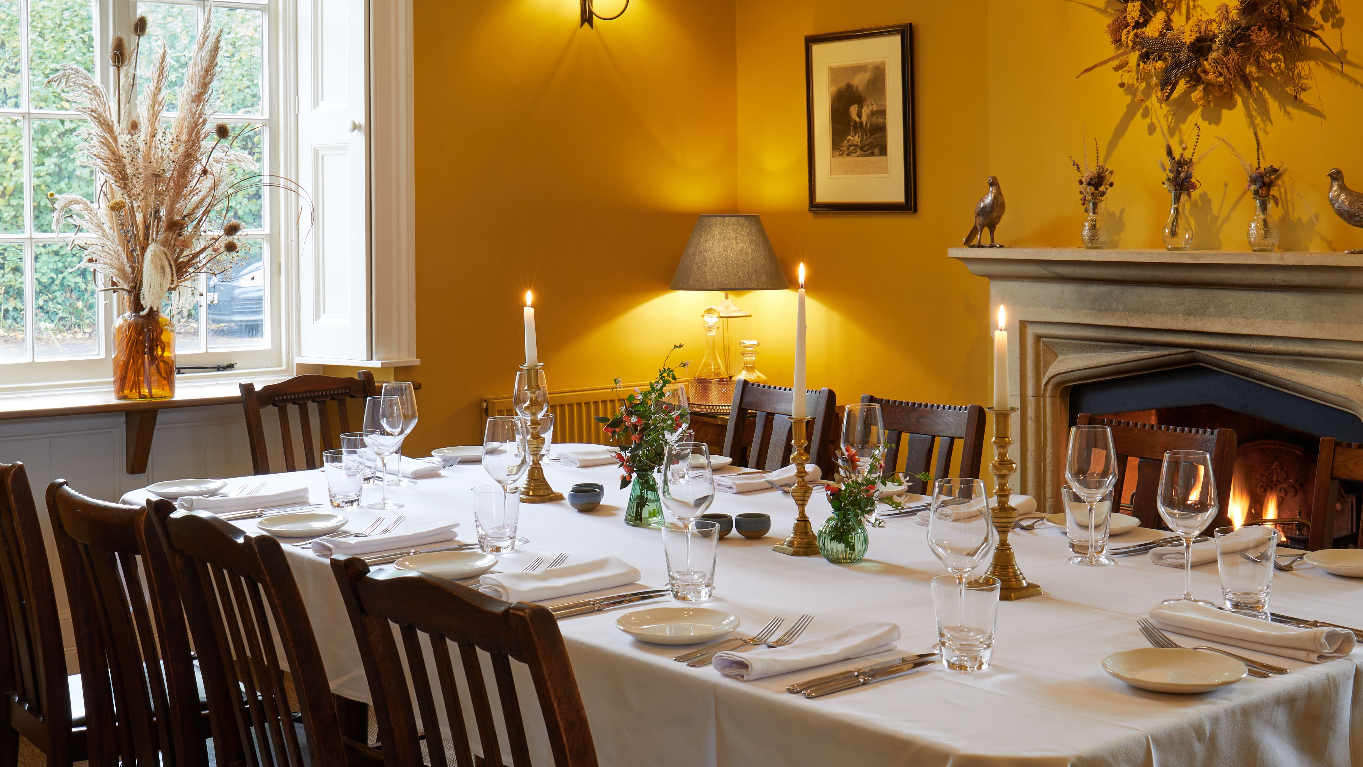 Elegant dining room with a set dinner table, lit candles, and a cozy fireplace.
