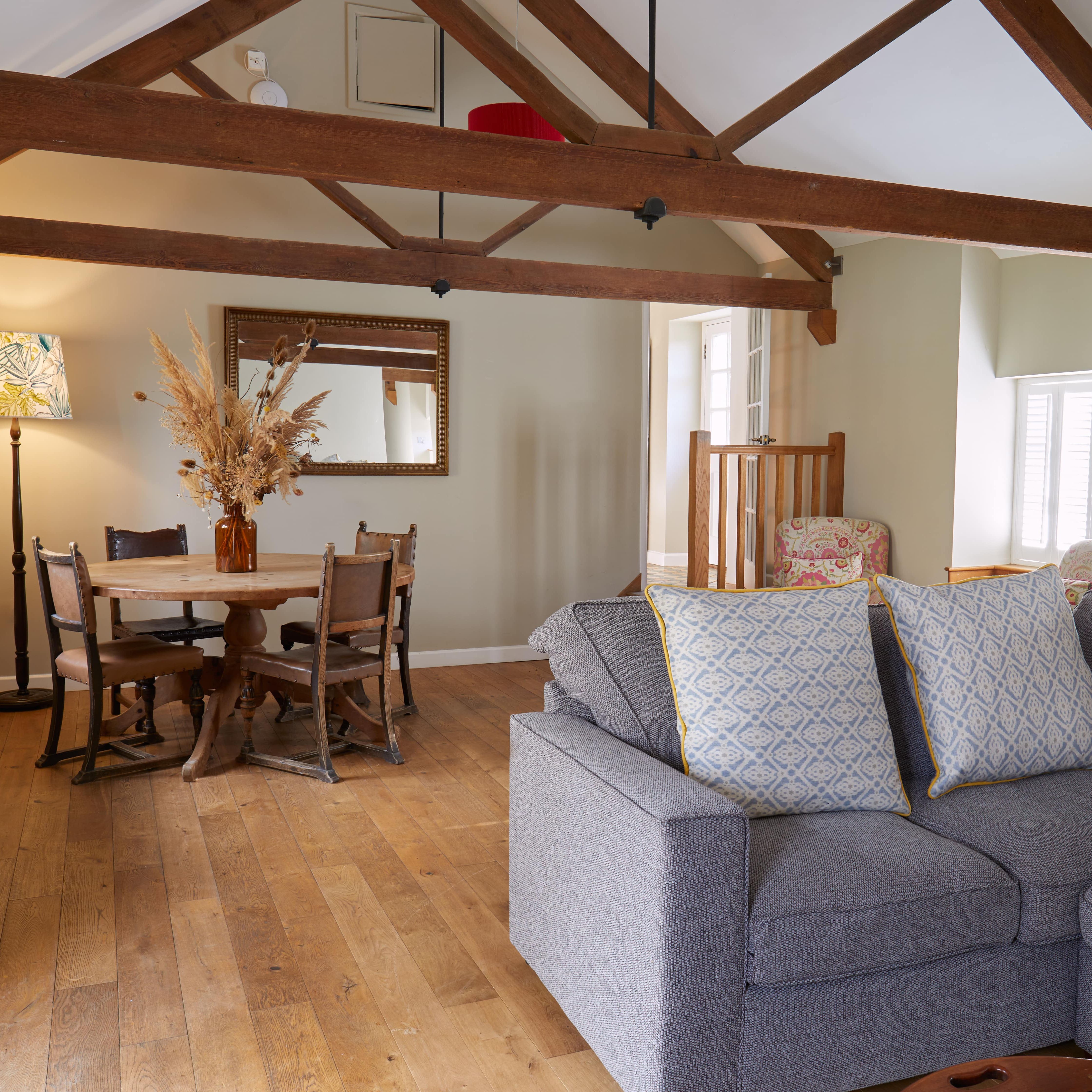 Cozy living room and dining area with exposed wooden beams, a gray sofa, and rustic furniture