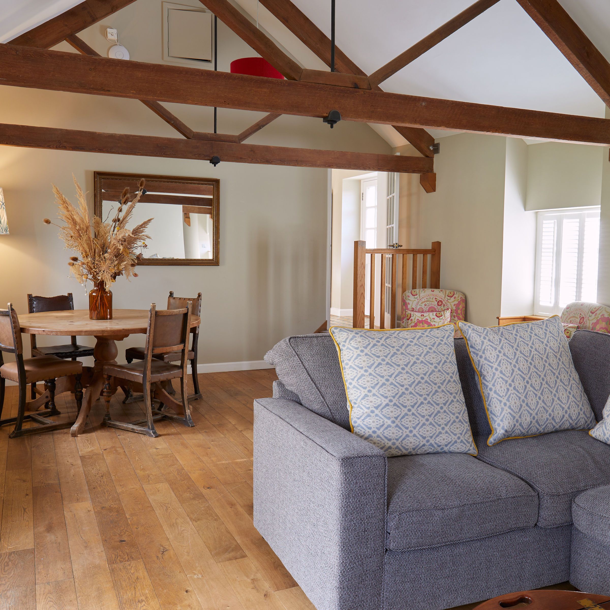 Modern rustic living and dining area with wooden beams, grey sofa, round table, and decorative lamp.