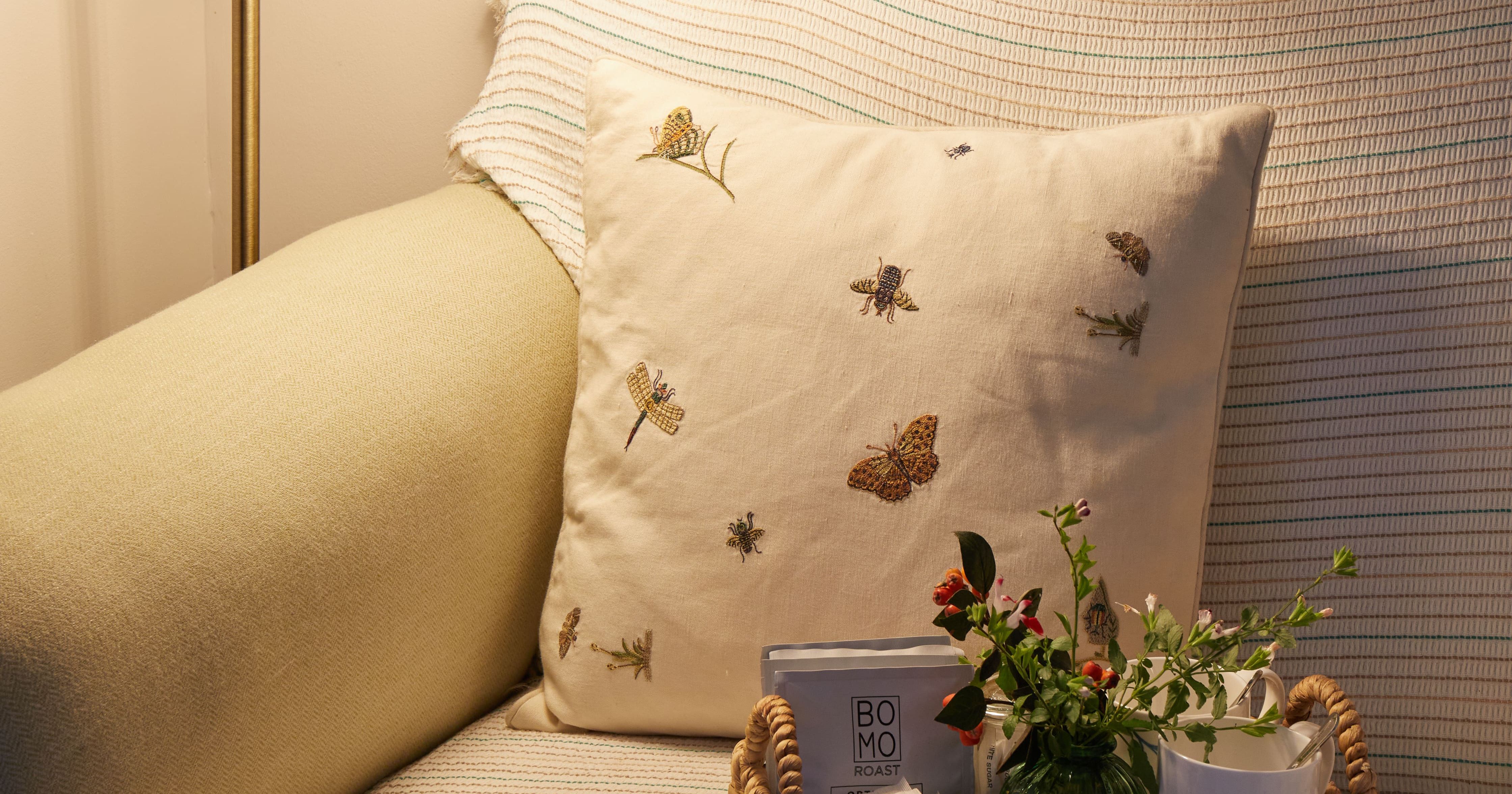 Cozy corner of a living room with a floor lamp, a couch with a decorative cushion, and a wicker tray with flowers and coffee items.