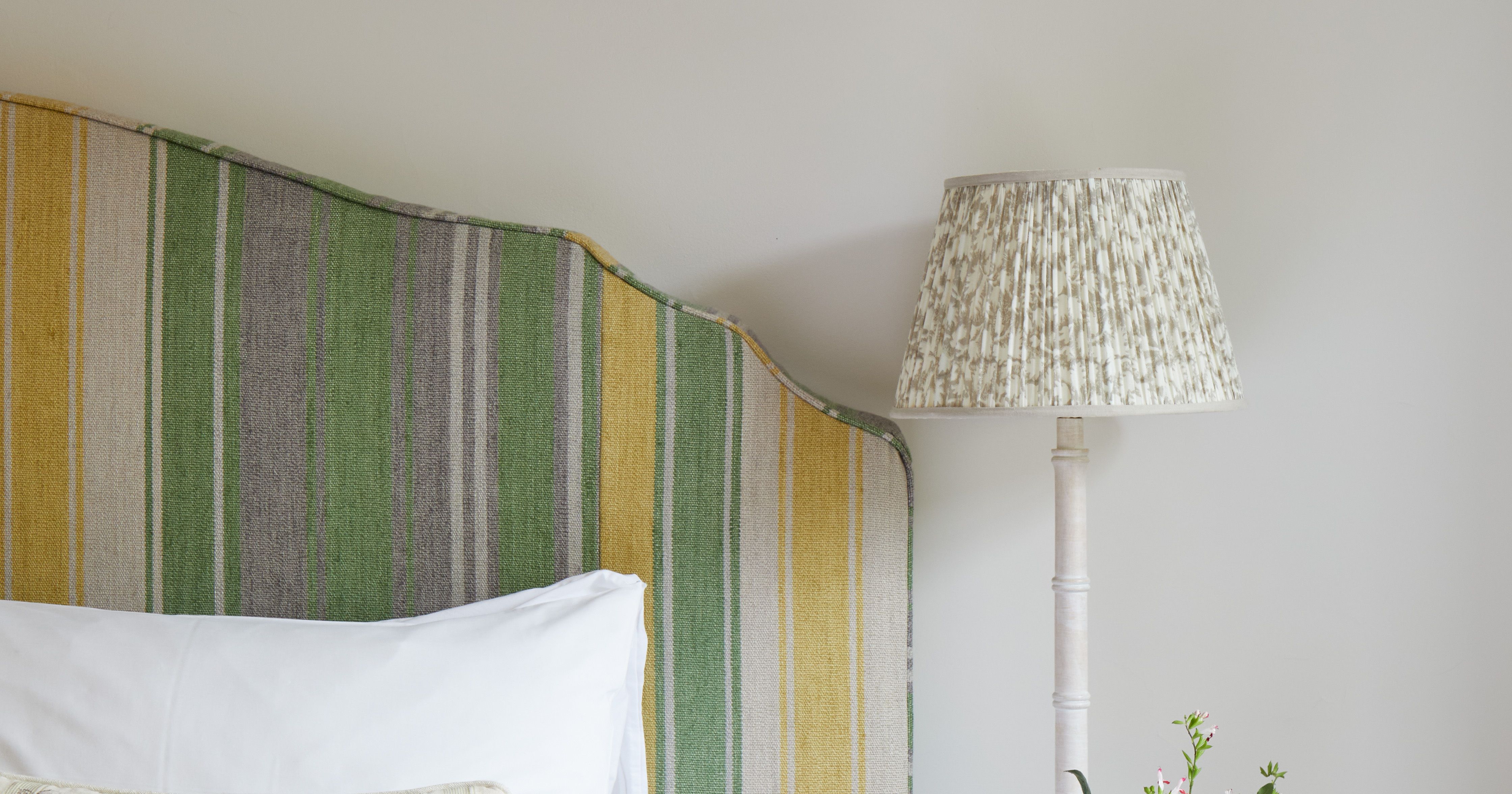 Cozy bedroom with striped headboard, white bedding, bedside table, lamp, and floral decor