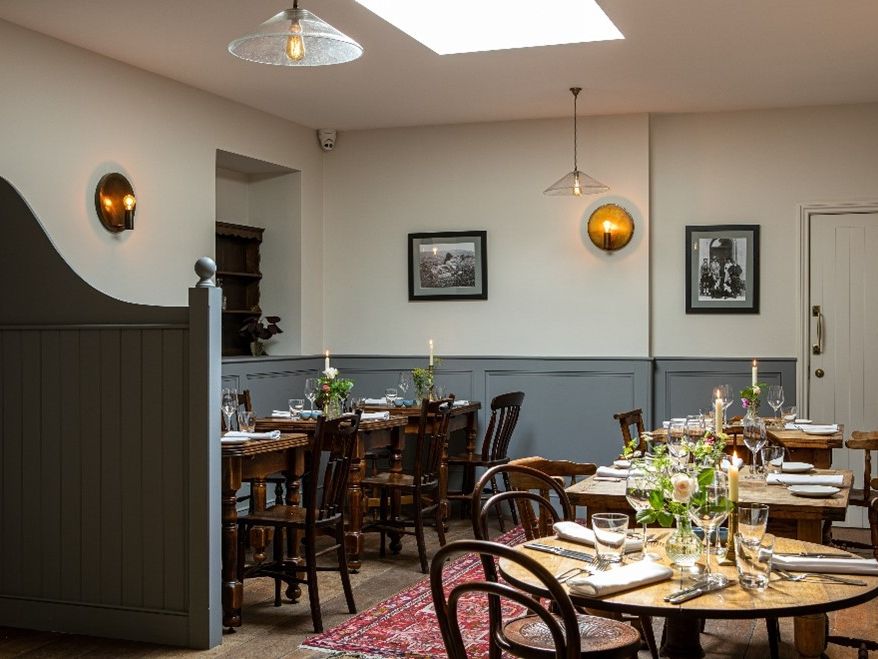 Cozy and elegantly set dining room with wooden tables, chairs, and lit candles.