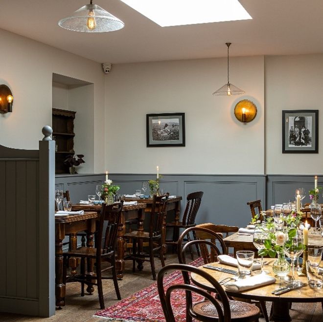 Cozy and elegantly set dining room with wooden tables, chairs, and lit candles.