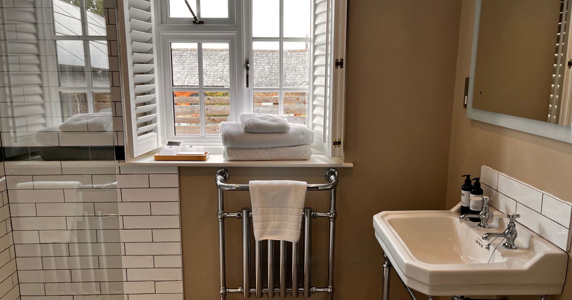 Modern bathroom with white tiled shower, sink, and window with shutters