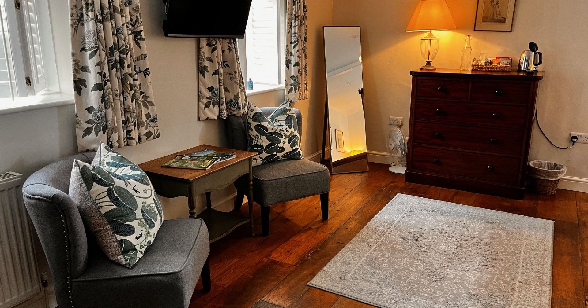 Cozy living space with two chairs, a dresser, TV, mirror, and lamp