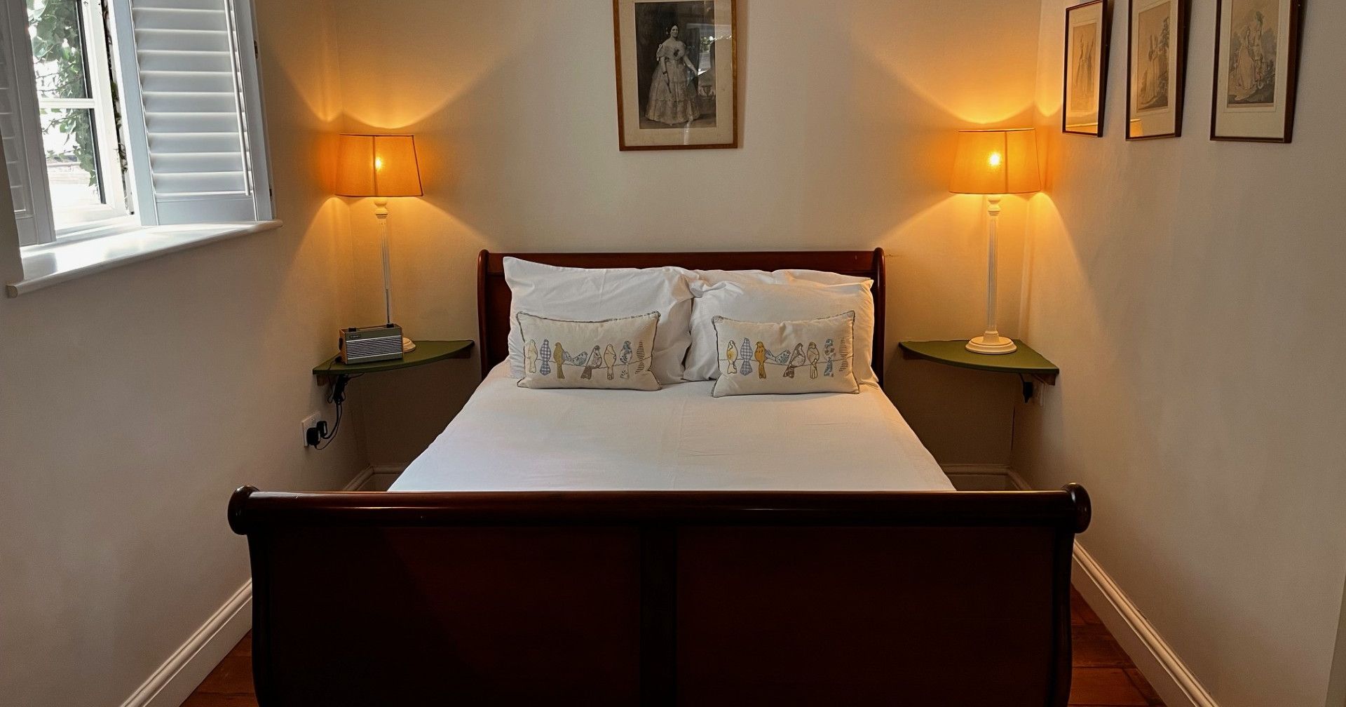 Cozy bedroom with wooden bed, white bedding, side lamps, and framed artwork on the walls.