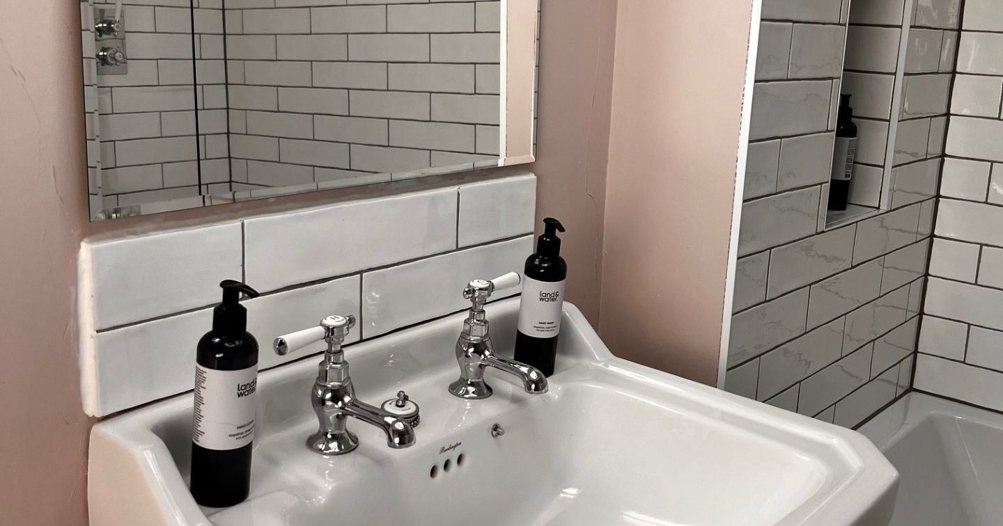 White bathroom sink with chrome taps, mirror above, and two black soap dispensers.