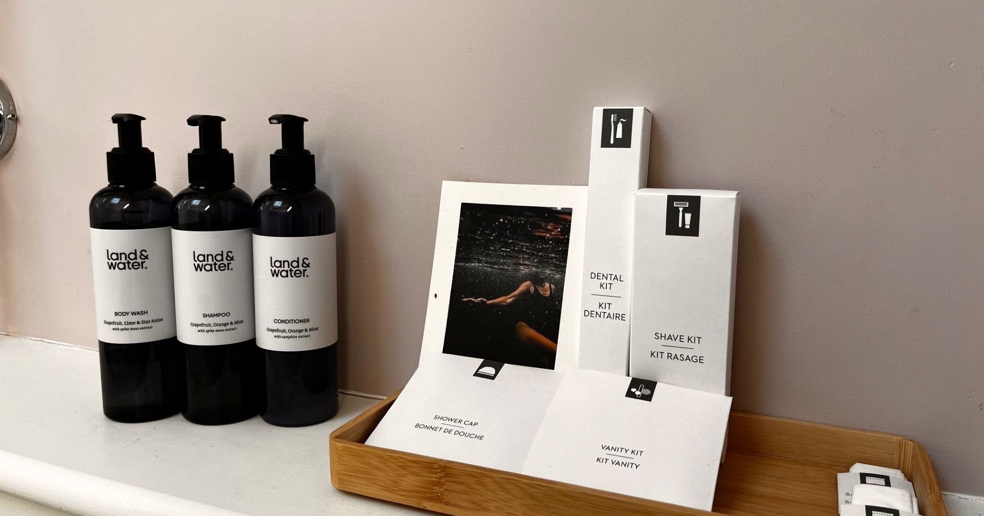 Assorted hotel toiletries including land&water body wash, shampoo, conditioner, and various kits on a tray