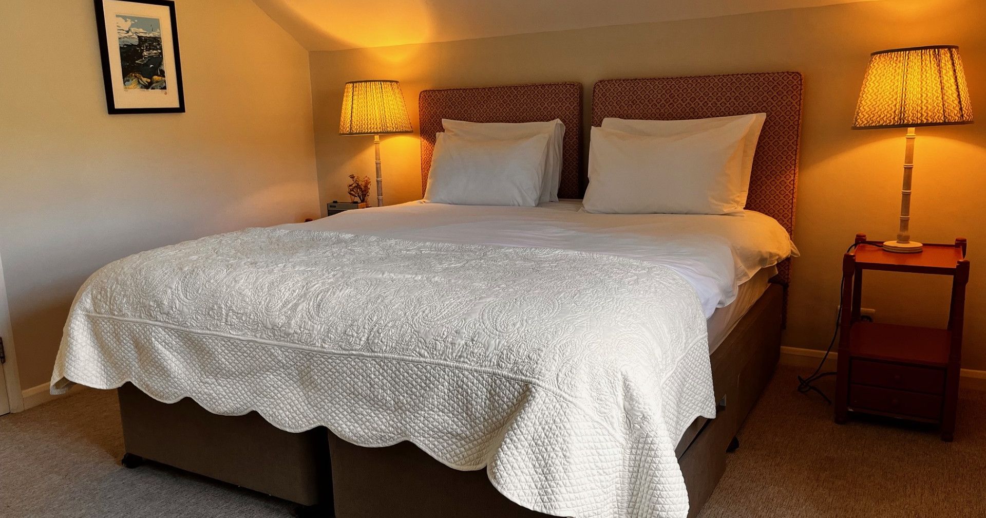 Cozy bedroom with a double bed, white quilt, two bedside lamps, and wall art.