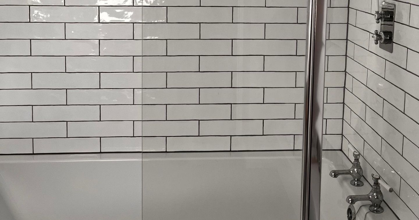 Modern bathtub with white subway tiles, black accent line, and chrome shower fixtures