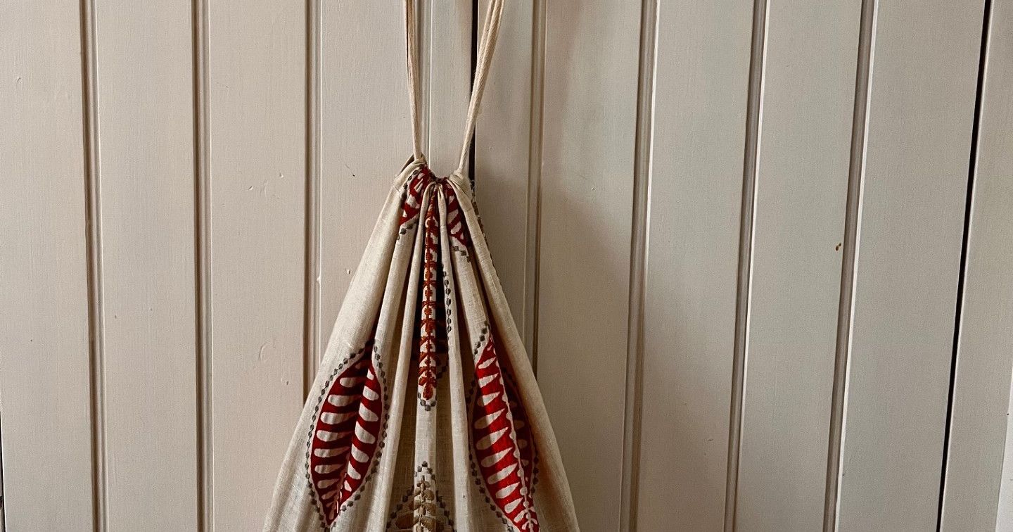 A fabric drawstring bag with leaf patterns hanging on brass knobs of a white paneled door.