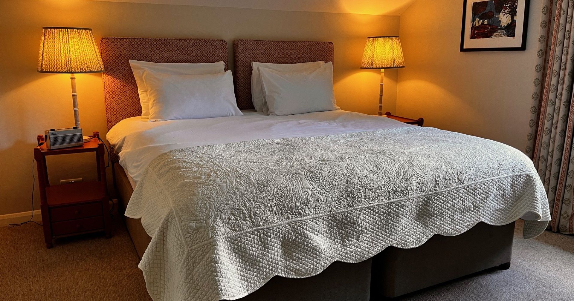 Cozy bedroom with a large bed, two bedside tables with lamps, and a framed painting on the wall.