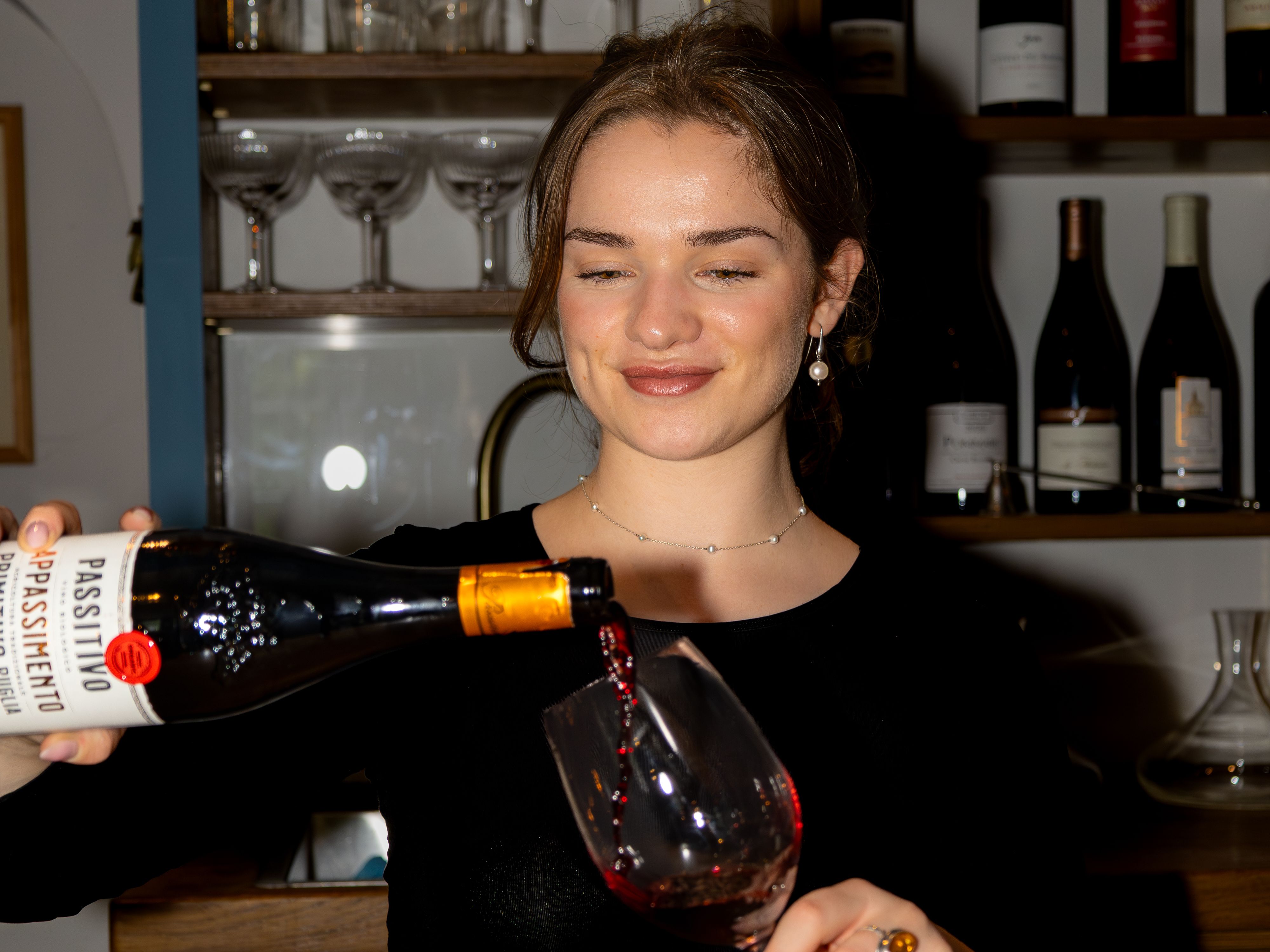Woman pouring red wine into a glass at a bar