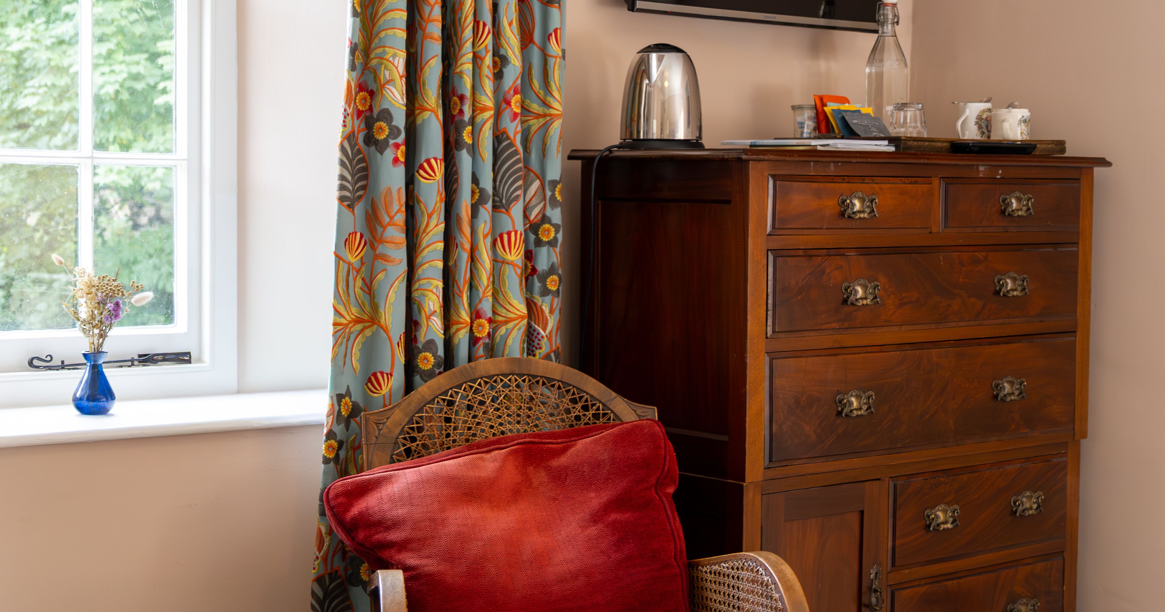 Cozy corner in a room with a red velvet chair, wooden chest of drawers, and a wall-mounted TV