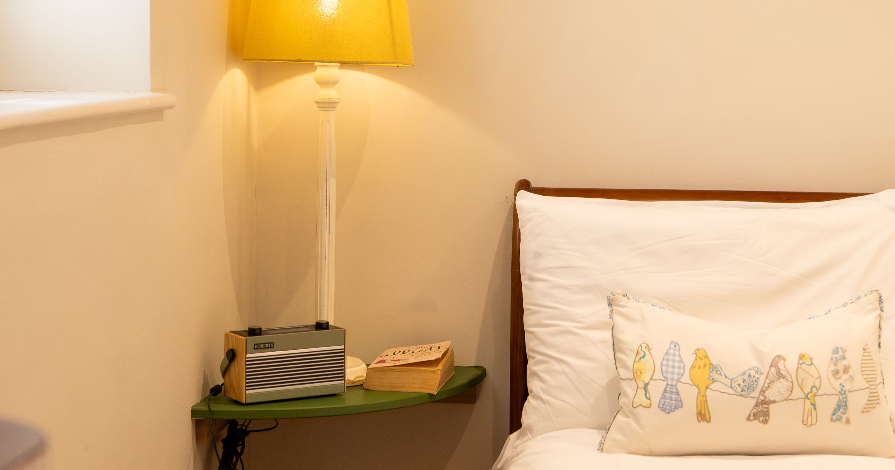 Cozy bedroom corner with lamp, radio, book, and bed with bird-patterned pillow