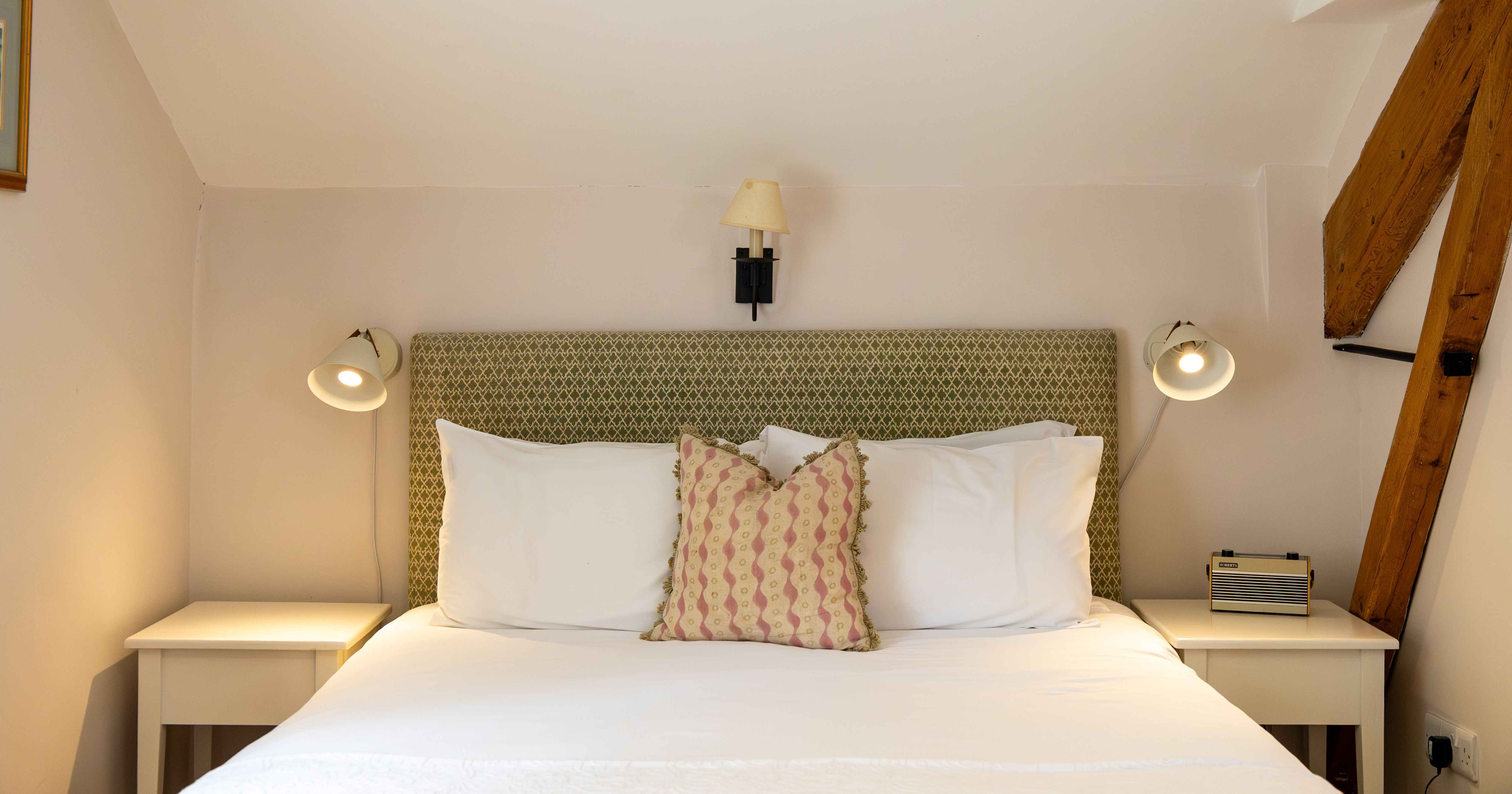 Cozy bedroom with a neatly made bed, white linens, and a decorative pillow, flanked by bedside tables and reading lamps.