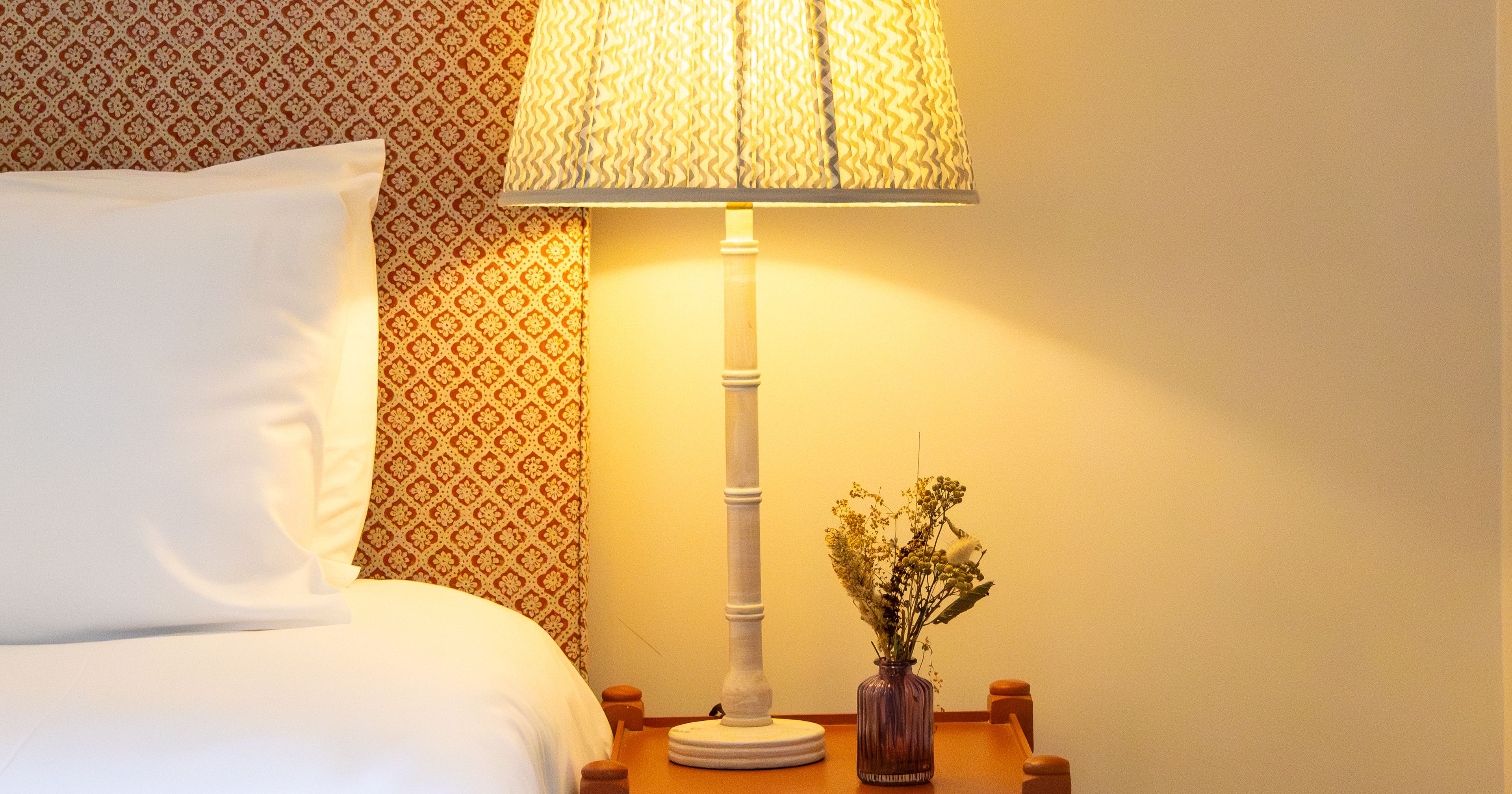 Bedside table with lamp and flowers next to a bed
