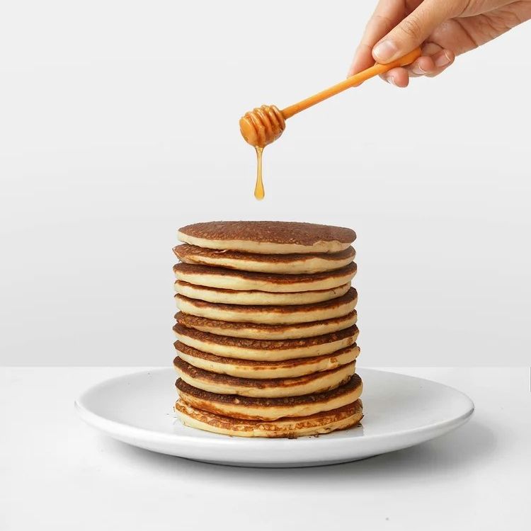 A stack of pancakes being drizzled with honey from a honey dipper held by a hand