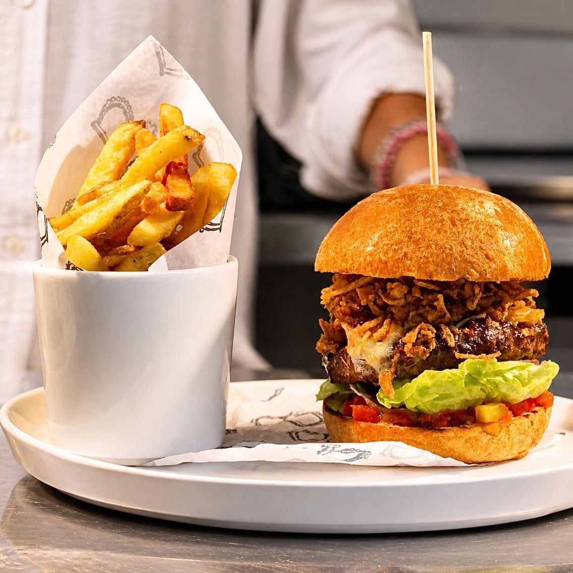 Gourmet burger with lettuce and sauce, served with chips in a white cup on a plate