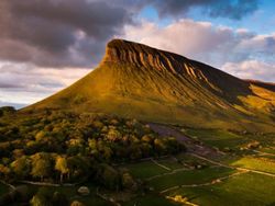 Scenic view of Benbulben mountain surrounded by lush greenery under a dramatic sky.