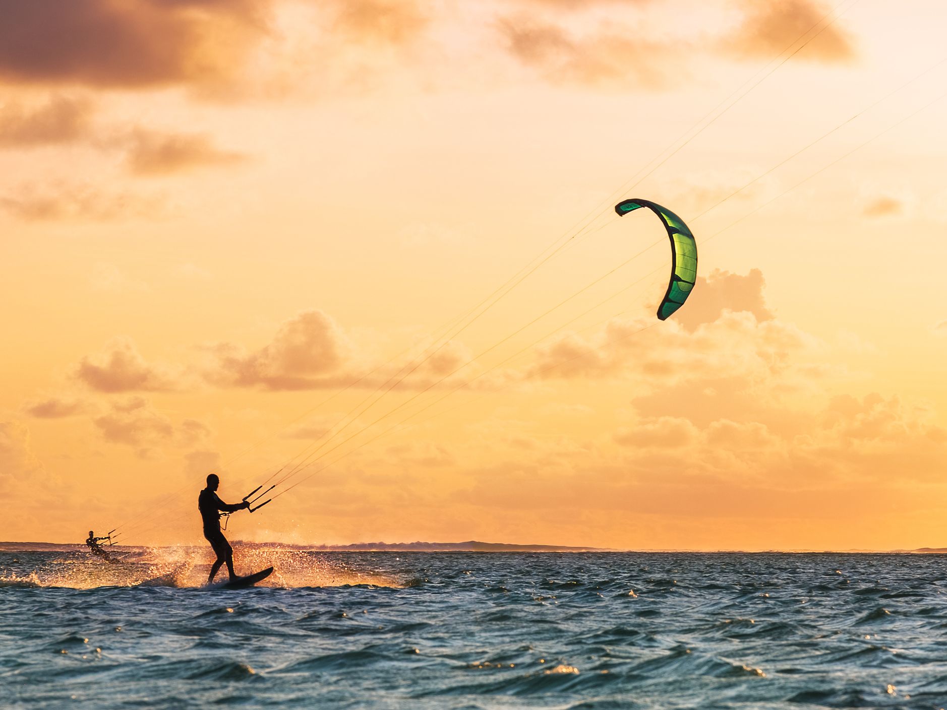 A kitesurfer glides across the water at sunset near the beaches in Sligo. The golden sky and gentle waves create a serene yet adventurous atmosphere, with clouds scattered above.
