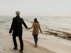 A couple walks hand in hand along the beaches in Sligo, dressed warmly against the cool weather. Gentle waves lap at the sandy shore as they enjoy a quiet moment by the sea.