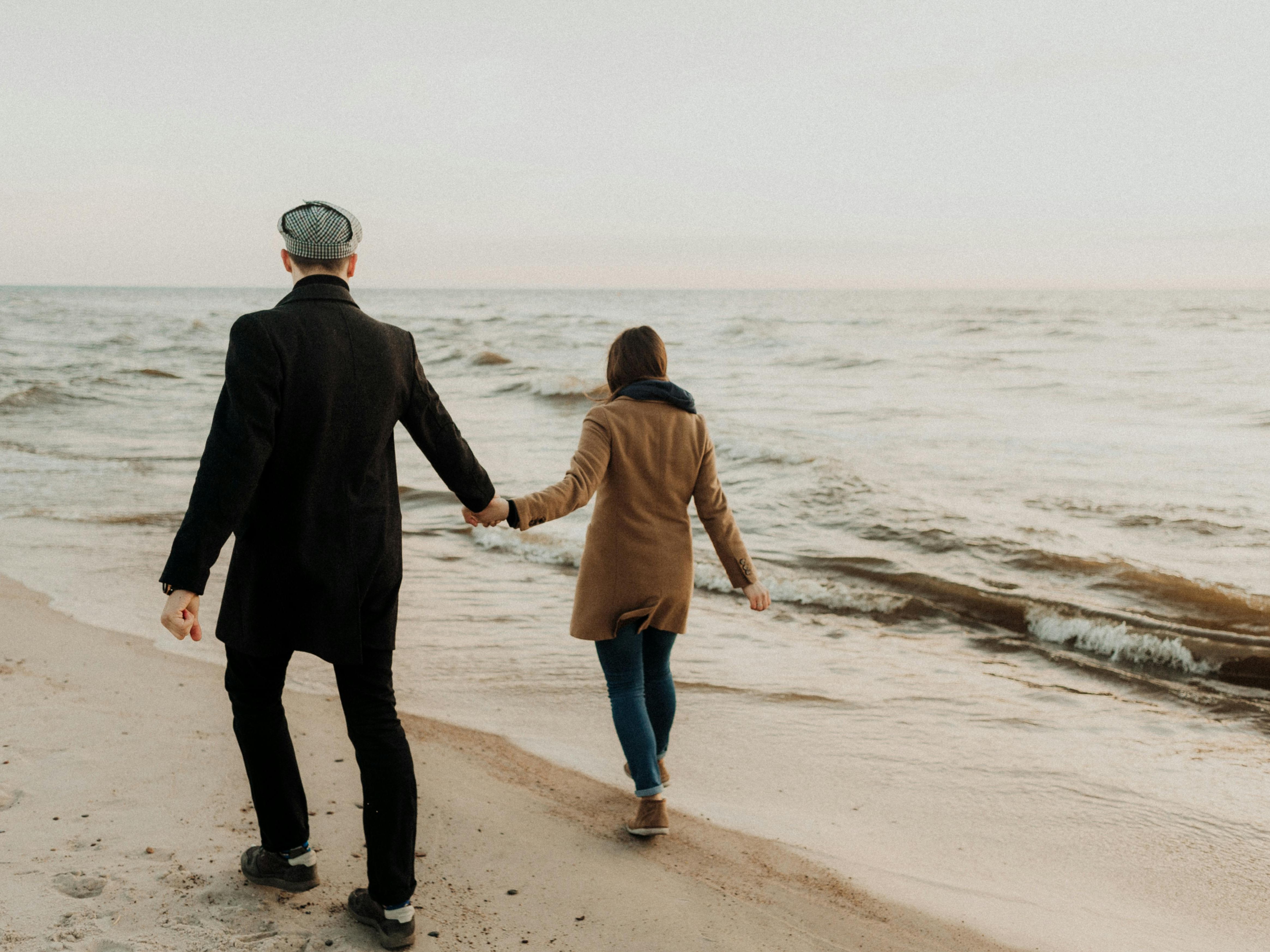 A couple walks hand in hand along the beaches in Sligo, dressed warmly against the cool weather. Gentle waves lap at the sandy shore as they enjoy a quiet moment by the sea.