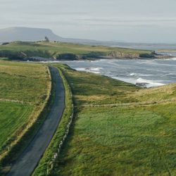 Scenic view of a road along the coastline in Sligo, with grassy hills and ocean waves.