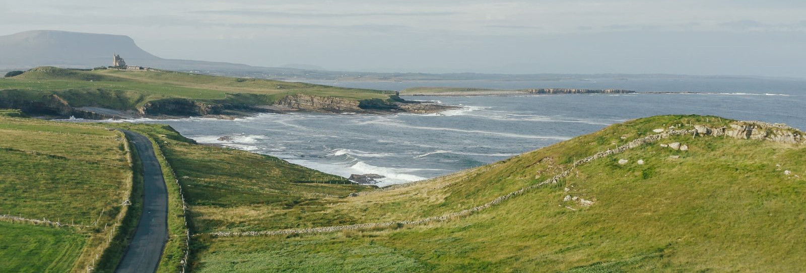 Scenic view of a road along the coastline in Sligo, with grassy hills and ocean waves.