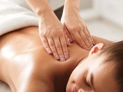 A woman enjoys a relaxing massage, lying face down with a soft smile as a therapist applies gentle pressure to her shoulders in a serene spa setting.
