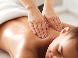 A woman enjoys a relaxing massage, lying face down with a soft smile as a therapist applies gentle pressure to her shoulders in a serene spa setting.