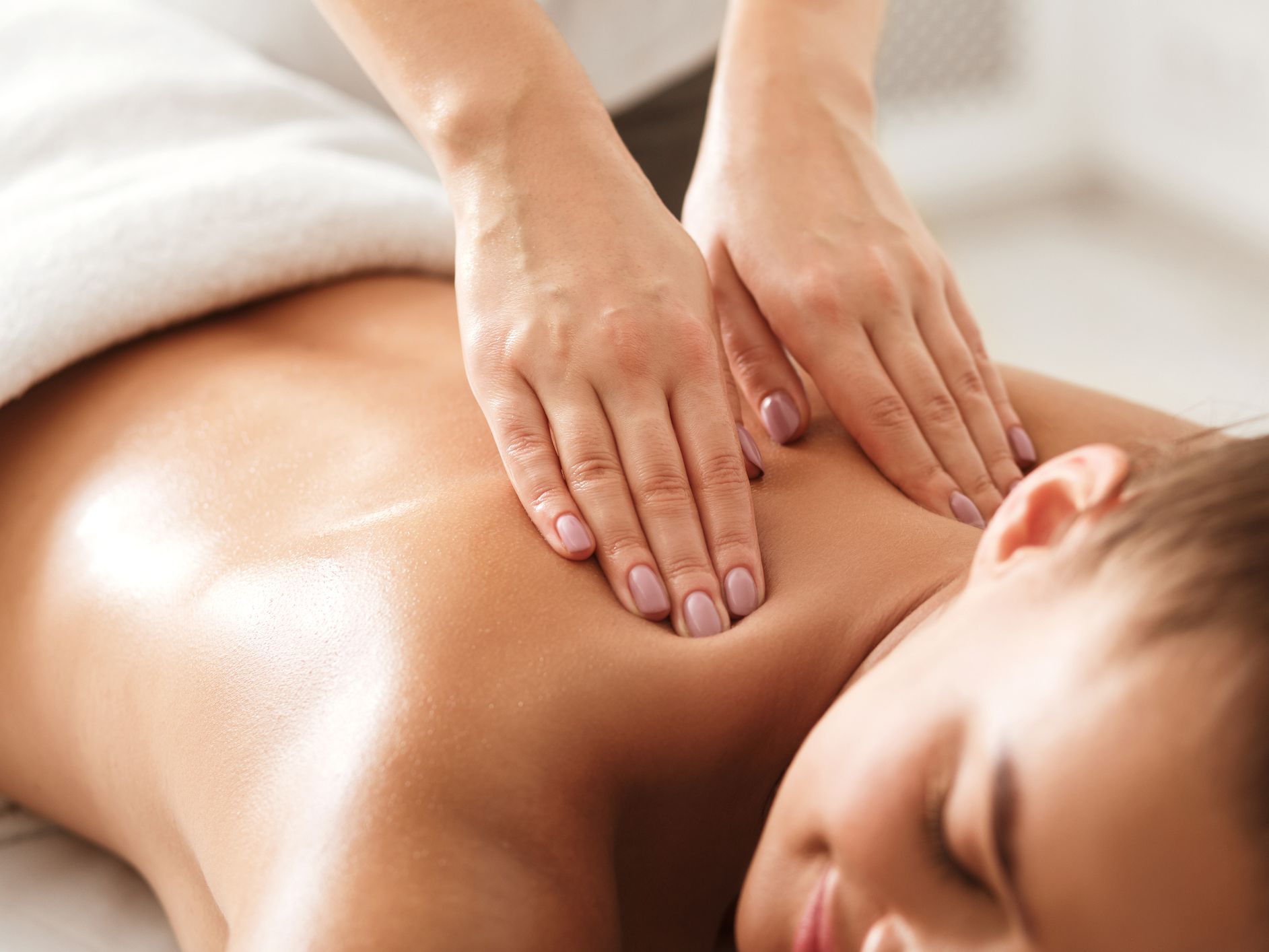 A woman enjoys a relaxing massage, lying face down with a soft smile as a therapist applies gentle pressure to her shoulders in a serene spa setting.