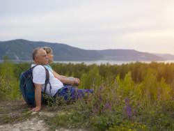 An elderly couple are sat among fresh greenery after a long walk, looking off to a beautiful sunset, one of the best Sligo walks