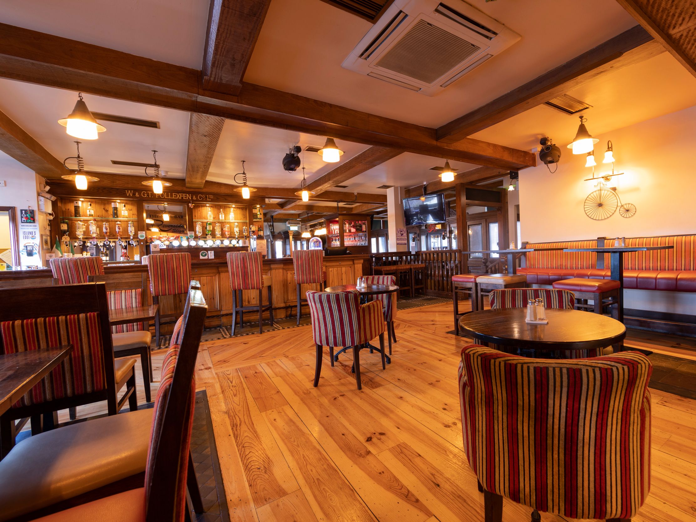 Warm and inviting pub interior with striped upholstered chairs and wooden tables, a wooden bar, and soft lighting.