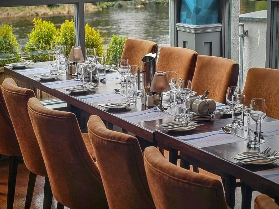 Elegant restaurant table set with glasses, plates, and cutlery by a window overlooking water.