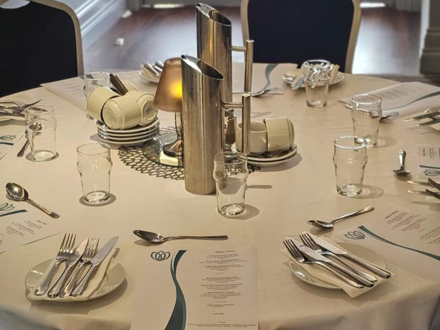 Elegant round dining table set with cutlery, glasses, menus, and stacked cup sets in a softly lit room.