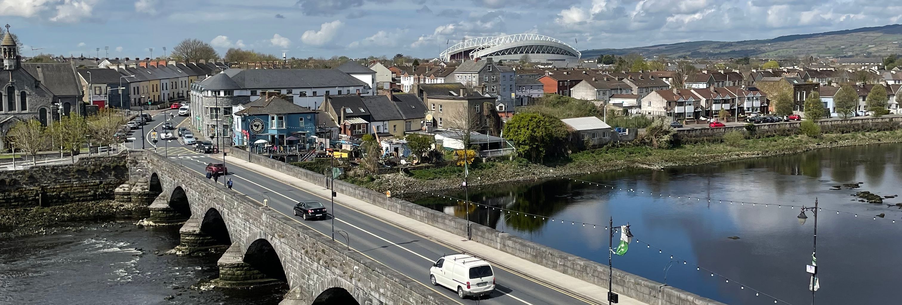Stone arched bridge crossing a river beside a town under a dramatic cloudy sky