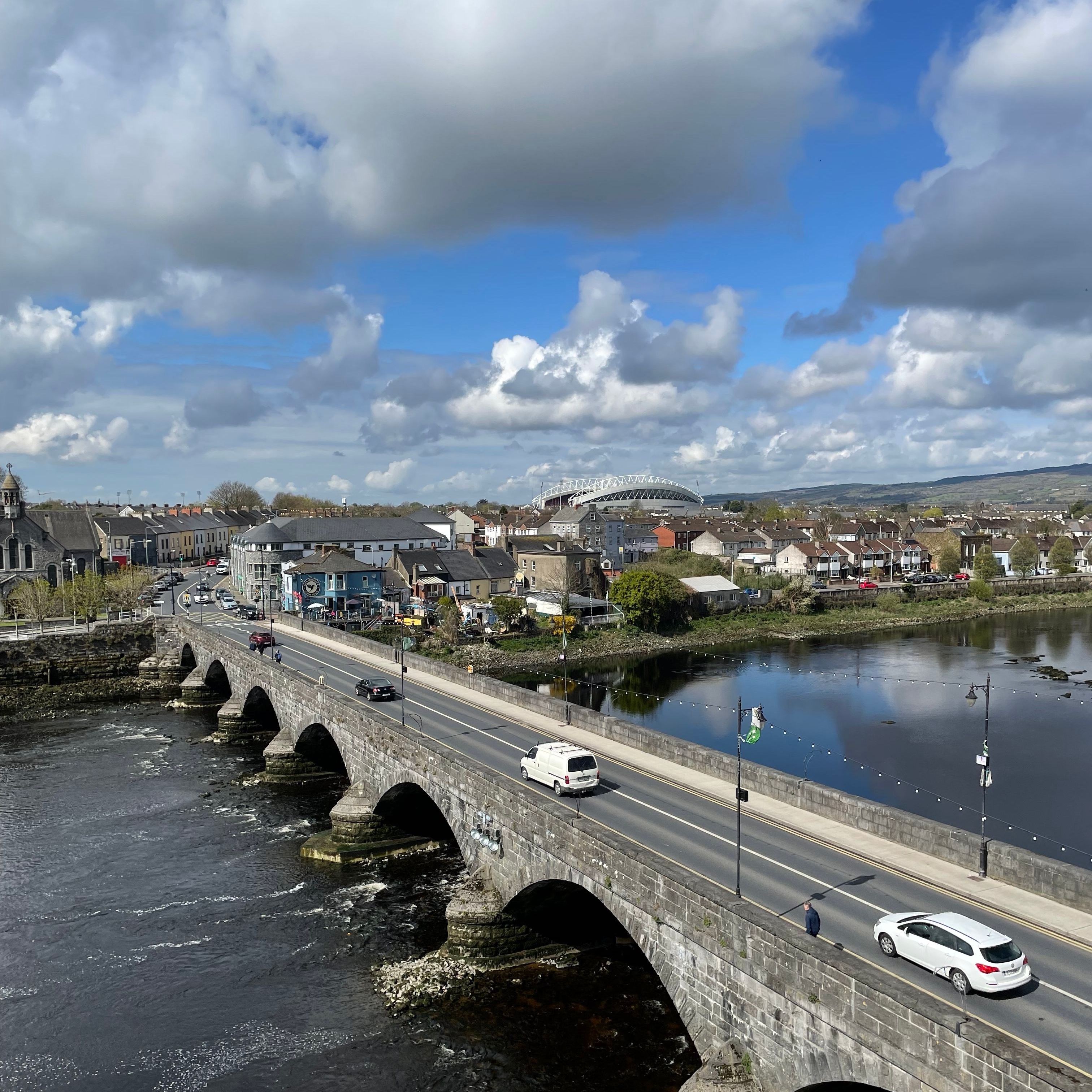 Stone arched bridge crossing a river beside a town under a dramatic cloudy sky