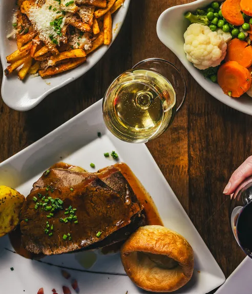 Sunday lunch spread with roast beef, Yorkshire pudding, vegetables and glasses of red and white wine