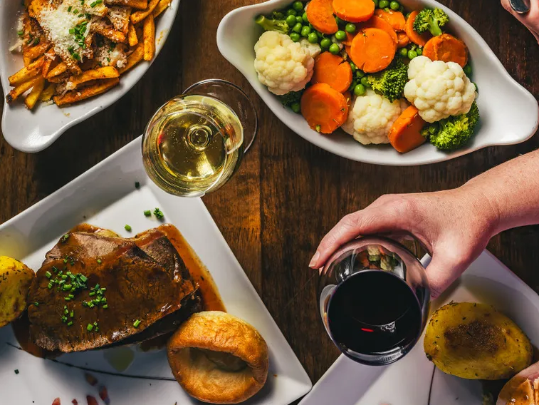 Sunday lunch spread with roast beef, Yorkshire pudding, vegetables and glasses of red and white wine