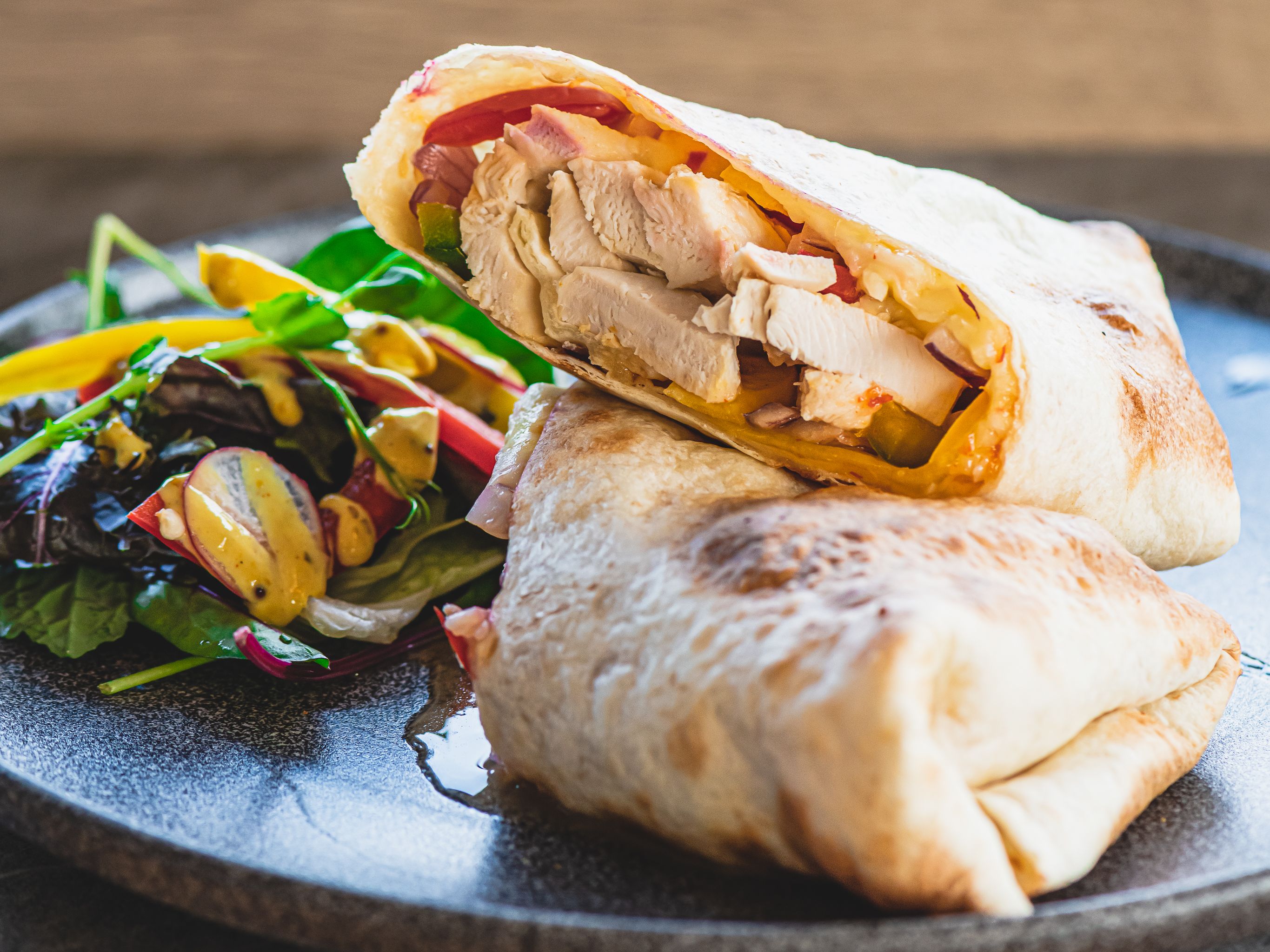Chicken wrap with salad and mustard dressing on a dark plate