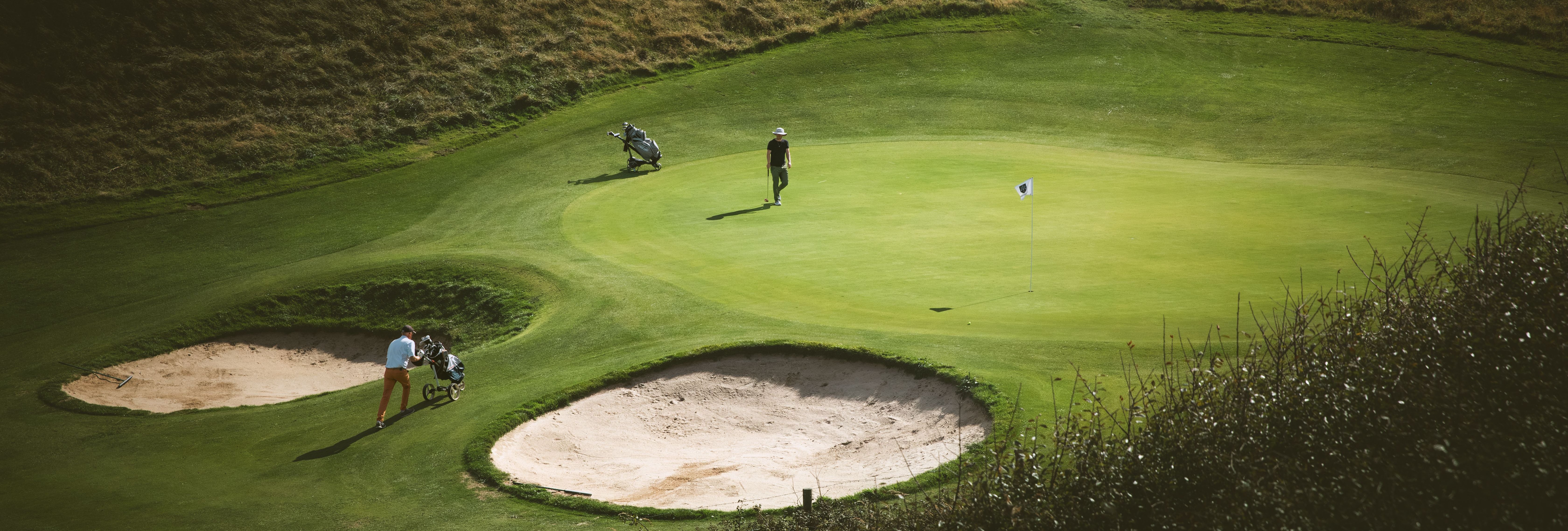 Golfers walking on a green beside sand bunkers on a hillside course