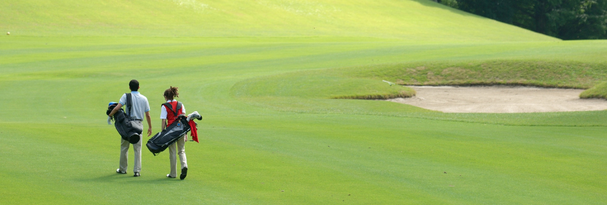 Two golfers walking across a green fairway carrying golf bags near a sand bunker