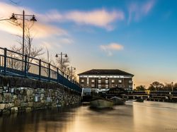 A peaceful riverside view with a stone wall, railings, and Riverside Hotel Sligo at sunset.