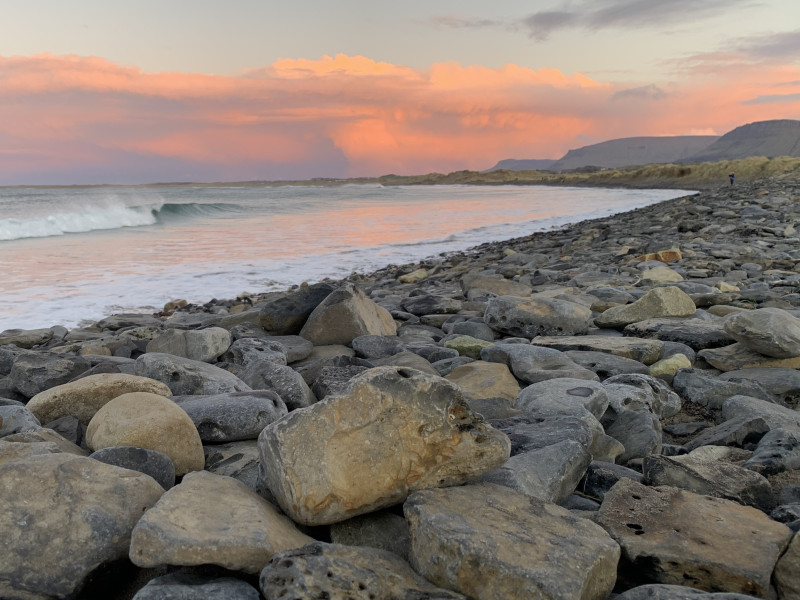 Pink sunset clouds over a rocky beach in Sligo, Ireland with waves crashing gently.
