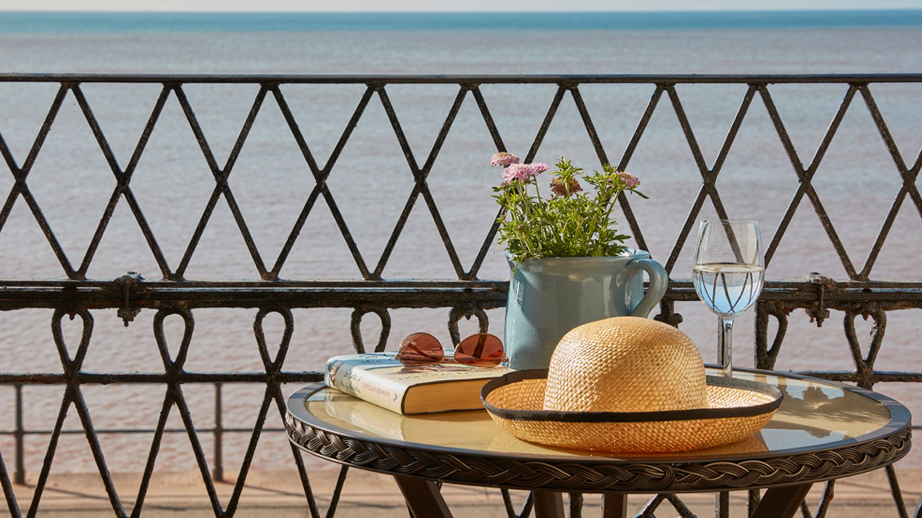 coffee table with book, hat and flowers overlooking sea front