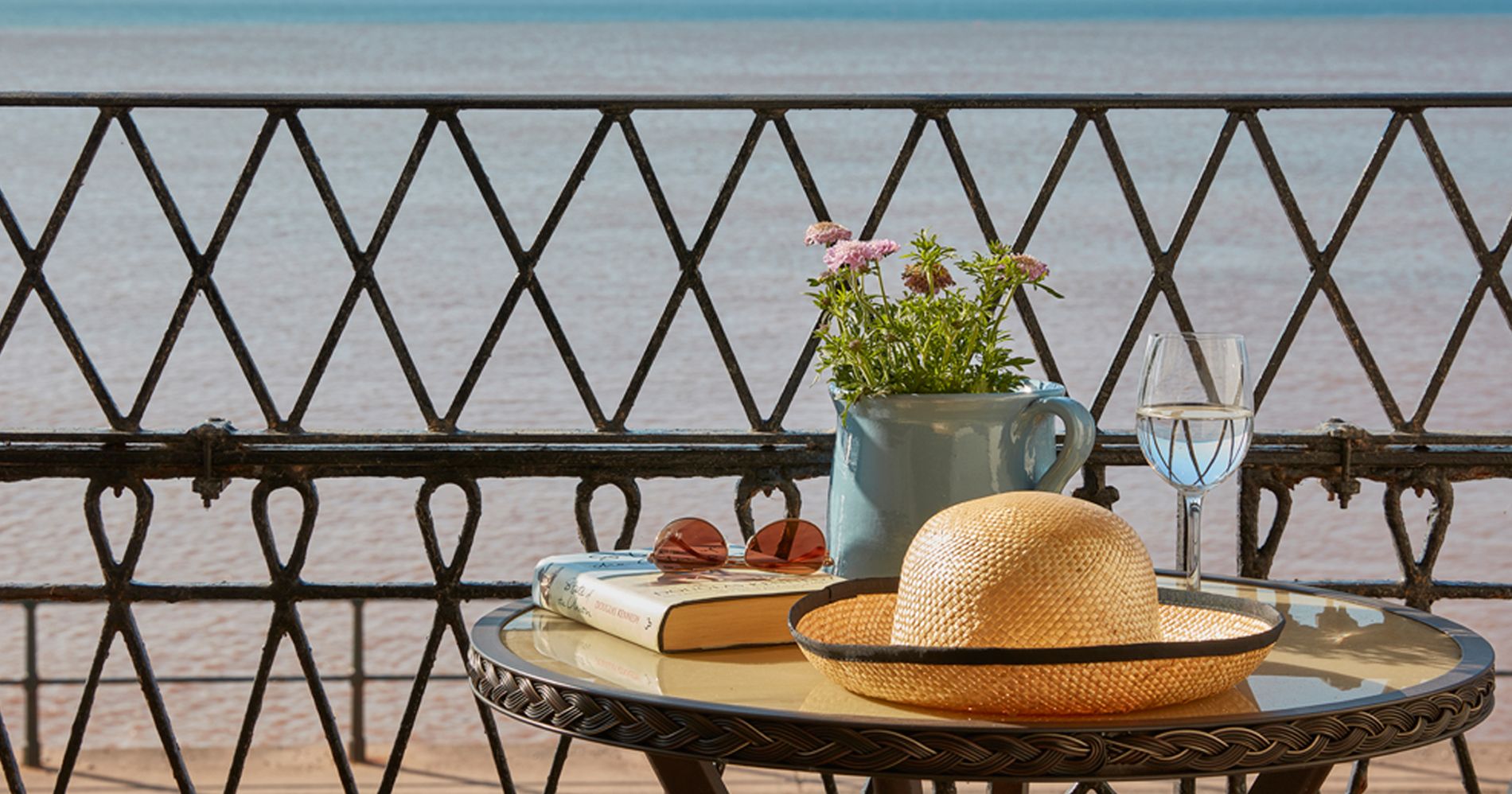 coffee table with book, hat and flowers overlooking sea front